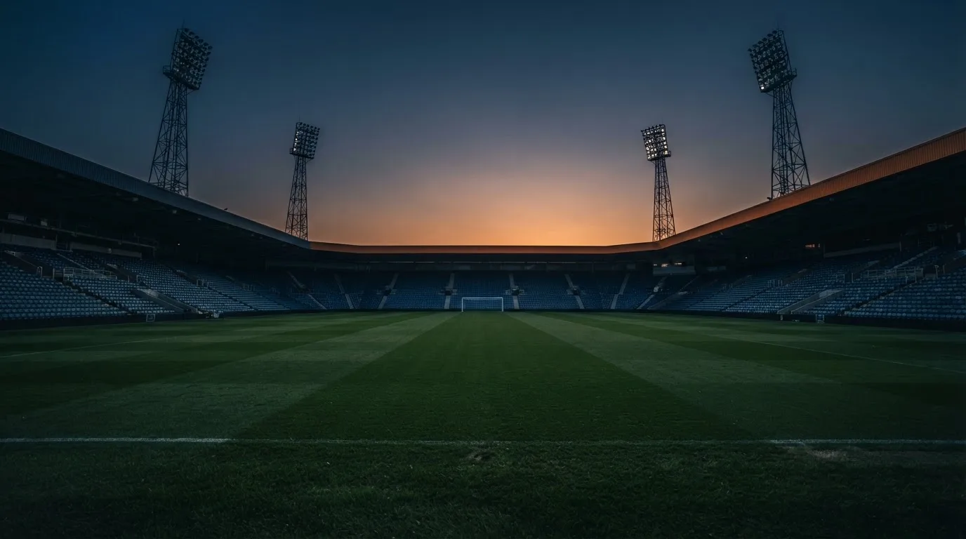 Een leeg voetbalstadion met lichtmasten bij schemering